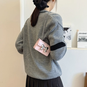 Chic pink leather mini crossbody bag with silver bow and chain strap on a model