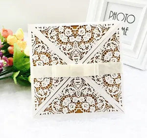 Detail of laser-cut white lace invitation card with elegant satin bow and floral patterns