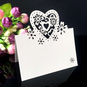 Elegant laser-cut heart and floral white wedding place card on reflective surface