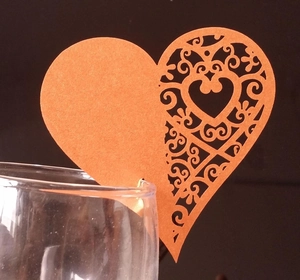 Close-up of laser-cut heart shaped orange place cards on the rim of a wine glass