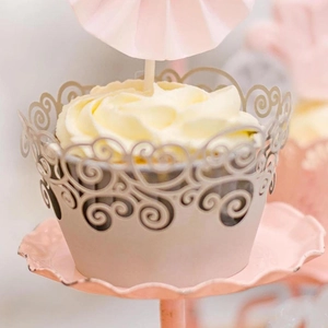 Elegant white laser cut cupcake wrappers with intricate scrollwork patterns for party decor