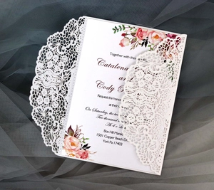 Close-up of laser-cut lace floral pattern on white wedding invitation with pink rose card