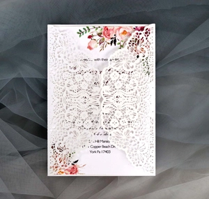 Close-up of intricate laser-cut lace wedding invitation with pink floral inner card