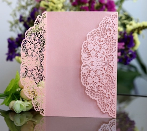 Detail of pink laser-cut wedding invitation featuring intricate floral lace hollow design