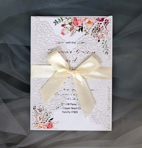 Detail of laser cut lace wedding invitation with pink flowers and a cream satin bow