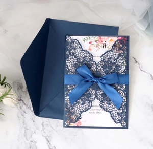 Detail of laser-cut lace wedding invitation with navy blue ribbon and pink floral card