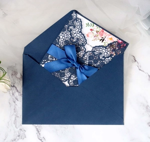 Detail of laser-cut navy blue lace wedding invitation with ribbon and floral card