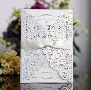 Elegant laser-cut wedding invitation in pearlescent white with silk satin ribbon and bow