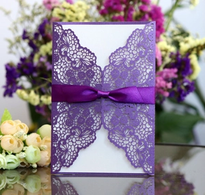 Detailed laser-cut lace wedding invitation with purple ribbon bow and white inner card