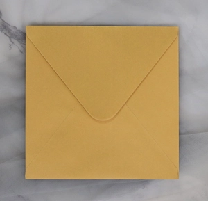 Flat lay of a mustard yellow square envelope with triangular flap on marble background
