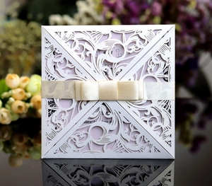 Macro shot of laser-cut white floral invitation with a champagne satin bow detail