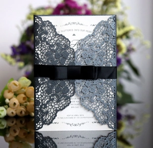 Detailed laser cut grey glitter wedding invitation with black satin bow and white card insert