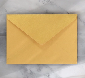 Close-up of a golden pearlescent paper envelope with V-flap on a marble background
