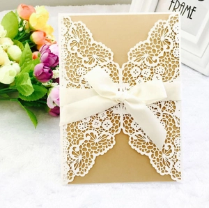 Detail of laser-cut white lace wedding invitation with kraft paper and white ribbon bow
