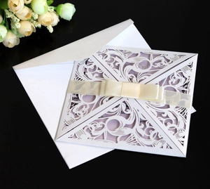 Detail of laser-cut hollow white wedding invitation with cream ribbon bow and envelope