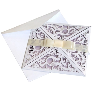 Laser cut white invitation card with intricate floral patterns and beige silk ribbon bow