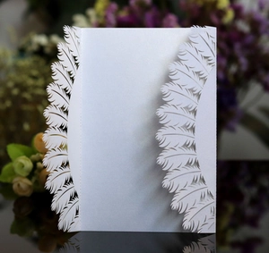 White laser cut feather invitation card with elegant bow on pearlescent paper