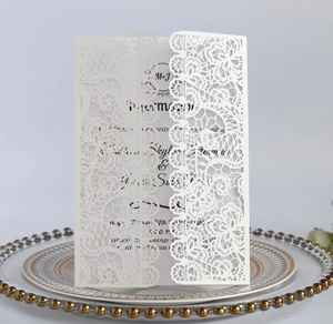 Detail of white laser-cut lace wedding invitation card with elegant initials on clear plate