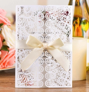 Lace laser-cut wedding invitation with satin ribbon and gold insert in romantic setting