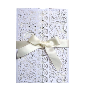 Intricate laser-cut lace wedding invitation with a cream satin ribbon bow and gold insert