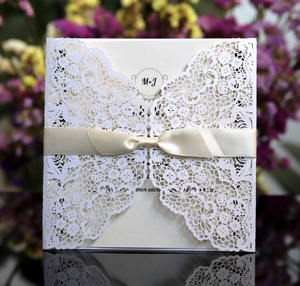 Macro detail of laser-cut lace wedding invitation with cream ribbon and floral background