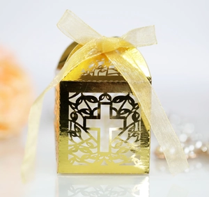 Detail of laser-cut gold cross favor box with delicate vine patterns and ribbon
