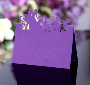 Purple laser-cut butterfly wedding place cards with heart motifs on black reflective surface