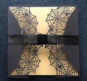 Detail of laser-cut spider web Halloween invitation with a matte gold insert and black ribbon