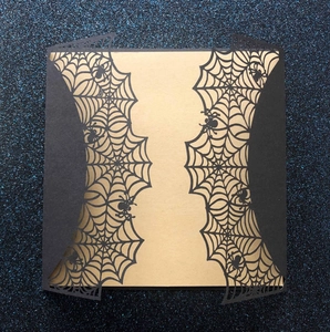 Detailed laser-cut black spider web invitation cover with a gold inner card insert