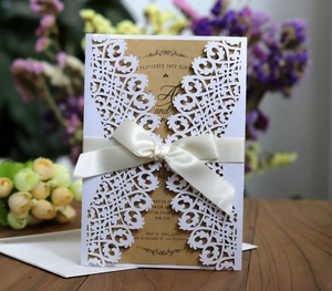 Close-up of laser-cut white wedding invitation with cream satin ribbon on wooden table