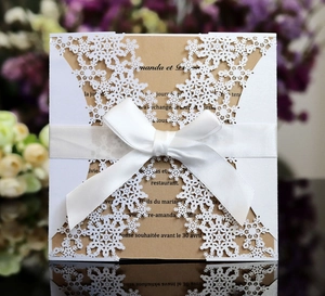 Detailed laser-cut snowflake wedding invitation with white ribbon and kraft inner card