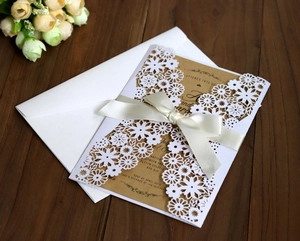 Détail d'invitation de mariage découpée au laser avec ruban crème sur fond en bois