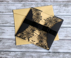 Laser-cut Halloween invitation with black spider web design and silk bow on wood background