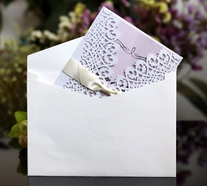 Elegant white laser-cut wedding invitation card with ribbon bow and envelope