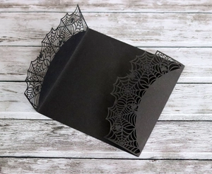 Detail of laser-cut black spider web invitation pocket on a white wooden background