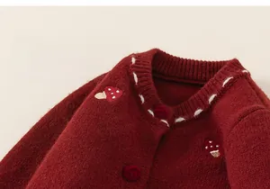 Detail of red knitted baby cardigan with mushroom embroidery and contrast stitching