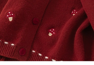 Detail of red knitted cardigan featuring embroidered mushroom pattern and round buttons