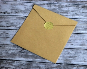 Brown kraft envelope with a gold 'Invitations' seal on a blue-grey wood background