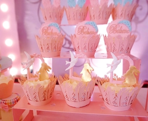 Detail of pink laser-cut lace cupcake wrappers and bird cake toppers on a dessert stand