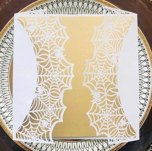Detail of laser-cut Halloween invitation with intricate spider web and gold inner paper