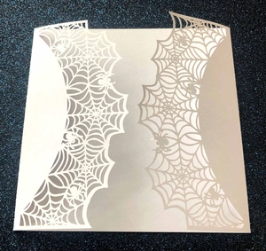 Detail showing laser-cut spider web pattern on white Halloween invitation card