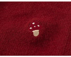 Detailed close-up of a delicate handcrafted mushroom embroidery on a dark red knit sweater