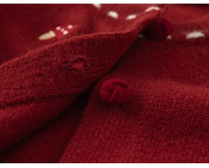 Close-up of red knitted cardigan with detailed mushroom embroidery and woven button