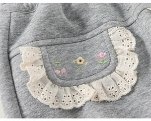 Détail d'un pantalon en tricot gris avec broderie florale et dentelle blanche sur la poche
