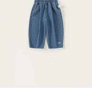 Dettaglio dei jeans da bambina con orlo in pizzo bianco e ricamo a fiocco