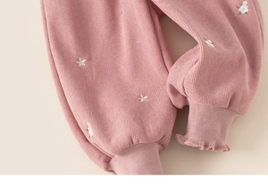 Detail of pink ribbed infant trousers featuring floral embroidery and ruffled cuffs