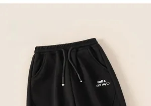 Detail of black winter sweatpants featuring elastic waist and embroidered slogan