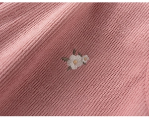 Detailed macro view of pink corduroy fabric featuring delicate daisy embroidery patterns