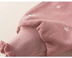 Detail of pink ribbed knit cuff with daisy embroidery and elegant ruffled edge