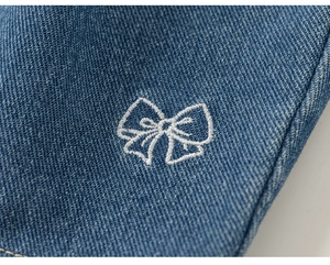 Dettaglio in denim blu con ricamo a fiocco bianco e finiture in pizzo per bambina